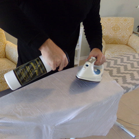 Person using a bottle and iron on an ironing board with yellow chairs in the background