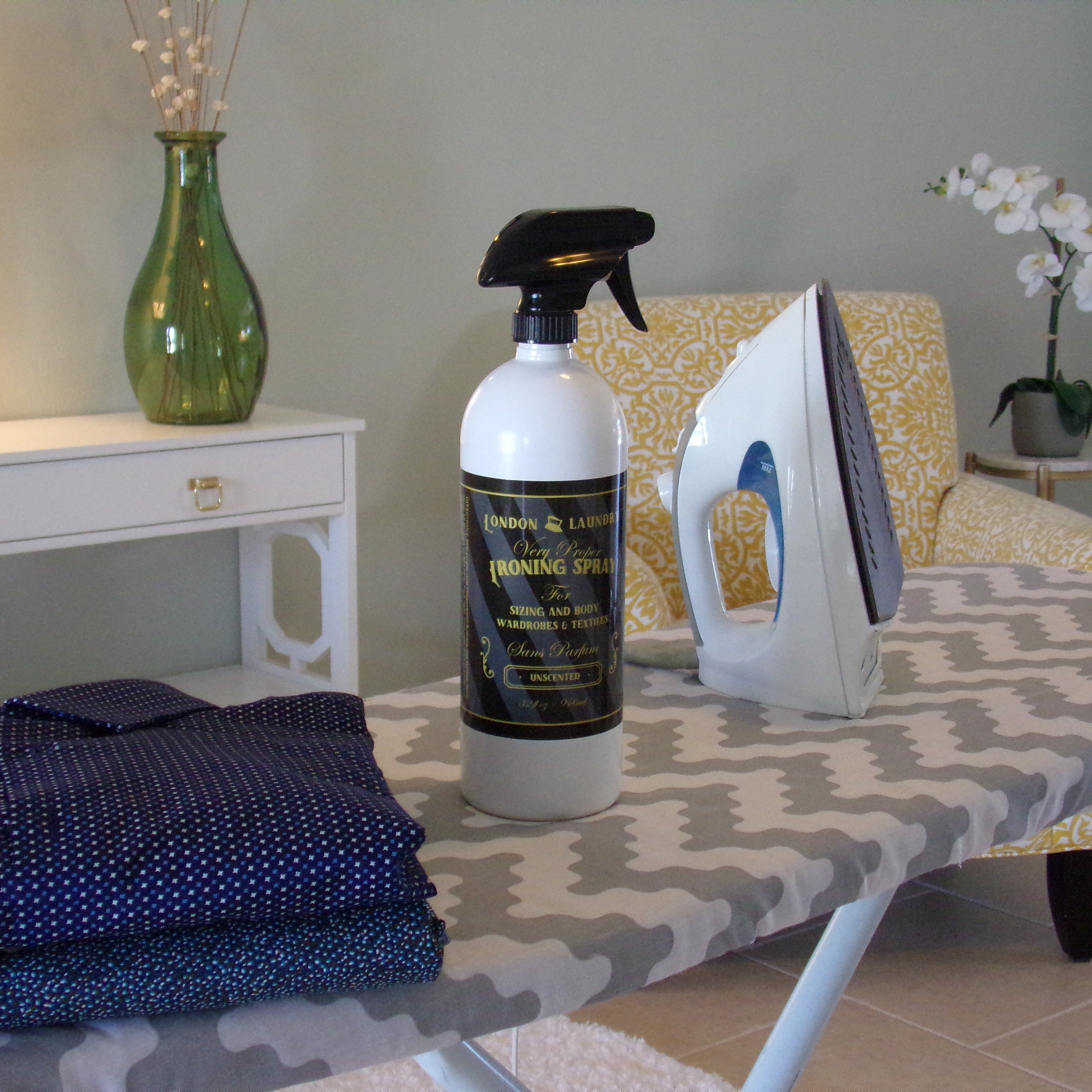 Iron, ironing board with folded clothes, and cleaning spray bottle on a table.